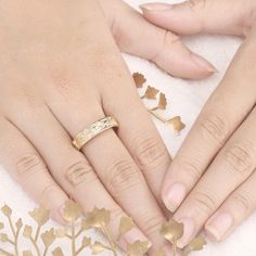 two hands holding each other with gold leaves on them and one hand wearing a wedding ring