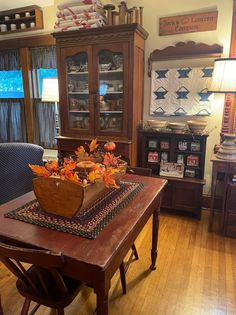 a wooden table topped with a basket filled with autumn leaves next to a blue chair