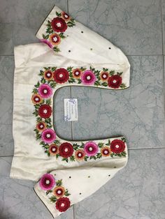 the letter e is decorated with flowers and leaves on white fabric, sitting on a tile floor