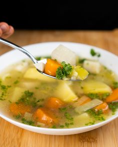 a spoon full of soup with carrots, celery and other veggies