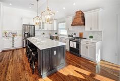 a large kitchen with white cabinets and wood flooring, including an island in the middle