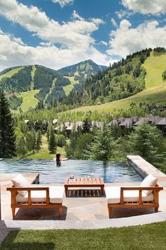 two wooden benches sitting on top of a lush green hillside next to a swimming pool