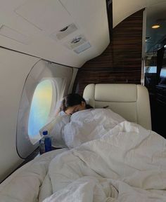 a woman laying in bed next to an airplane window with her head on the pillow