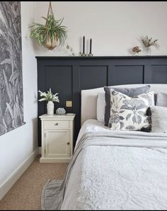 a white bed sitting next to a wall with plants on top of it and a night stand in front of it