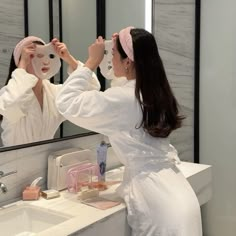 a woman in a bathrobe is looking at her reflection in the mirror as she brushes her hair