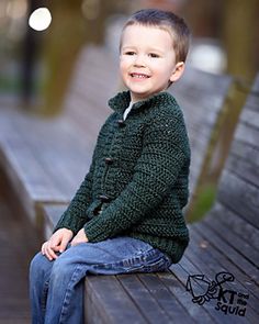 a young boy sitting on top of a wooden bench wearing a green sweater and jeans