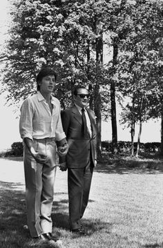 two men walking in the grass next to each other with trees in the back ground