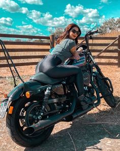 a woman sitting on top of a motorcycle in the dirt near a fence and wooden posts