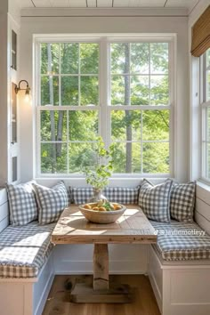 a wooden table sitting under a window next to a bench with pillows on top of it