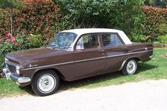 an old brown and white car parked on the side of a road in front of some bushes