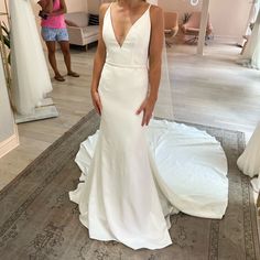 a woman standing in front of a mirror wearing a white wedding dress with a low v neckline