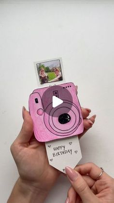 two hands holding up a pink camera with a happy birthday card attached to the front