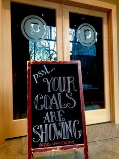 a chalkboard sign sitting in front of a door that says, post your goals are showing