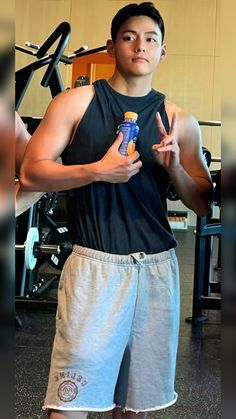 a young man is holding a bottle and posing for the camera in front of a gym machine