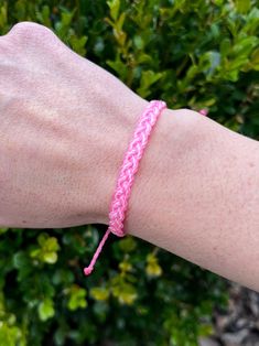 a person's arm with a pink bracelet on top of it and bushes in the background