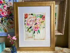 there is a vase with flowers in it next to some framed pictures and other items