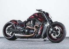 a red and black motorcycle parked on top of a cement floor next to a white wall