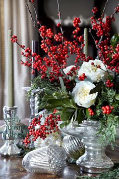 a vase filled with red berries and white flowers on top of a table next to candles