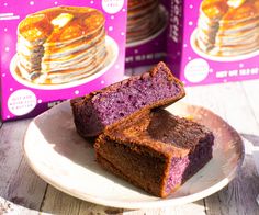 purple cake sitting on top of a white plate next to two boxes of blueberry pancakes