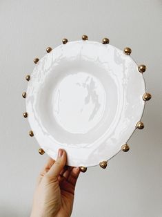 a person holding a white and gold plate with balls on the rim, in front of a gray wall