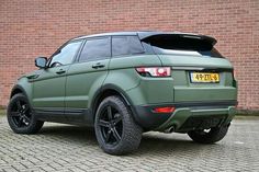 a green range rover parked in front of a brick wall