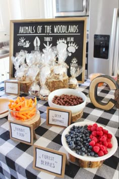 a table topped with bowls filled with fruit and veggies next to a sign that says animals of the woodlands