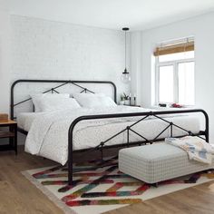 a bedroom with a bed, ottoman and rug on the floor in front of a window