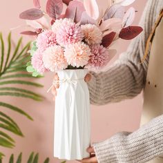 a person holding a white vase filled with pink flowers