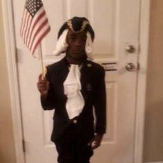 a young boy dressed in black and white holding an american flag on his head while standing in front of a door