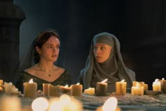 two women sitting at a table with candles in front of them and one woman wearing a headscarf