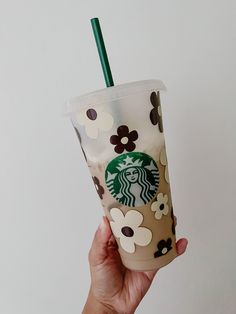 a hand holding a starbucks cup with a green straw and flower design on the lid