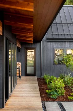 a person walking down a wooden walkway next to a building with black siding and windows