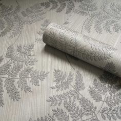 a roll of fabric sitting on top of a bed next to a wallpaper covered in leaves