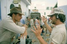 two men with hats on talking to each other in front of a group of people