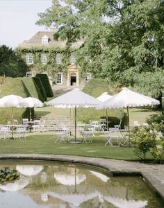 tables and umbrellas are set up in front of a large house on the lawn