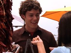 a young man standing next to a woman at an outdoor market holding something in his hand