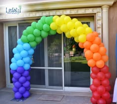 an arch made out of balloons in front of a window with the colors of rainbow