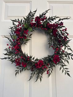 a wreath with red flowers and green leaves hangs on the front door's white paneling