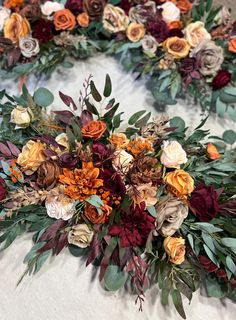 an arrangement of flowers and foliage on a white tablecloth with red, orange, yellow, and green leaves