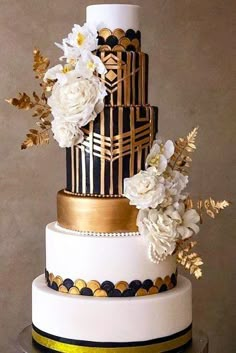 a three tiered cake with white flowers and gold leaf decorations on it's sides