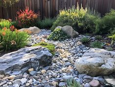 a garden with rocks and plants next to a fence