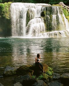 a woman sitting on top of a rock next to a waterfall