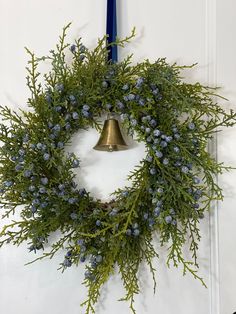 a wreath is hanging on the door with a bell in front of it and blue flowers