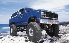 a blue lifted truck on rocks by the ocean