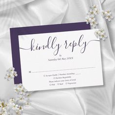 a white and purple wedding reception card with flowers on the bottom, in front of a satin background