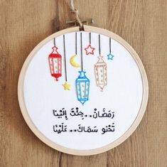 a cross stitch pattern with arabic writing and lanterns hanging from strings on a wooden surface