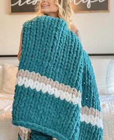 a woman wrapped up in a blue and white knitted blanket on top of a bed