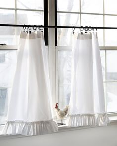 two white curtains with ruffles hanging from them in front of a window sill