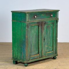 an old green cabinet with two doors and wheels on the bottom, sitting on a wooden floor