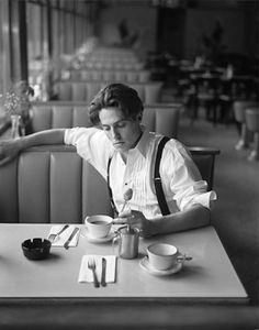 a man sitting at a table in front of a cup and saucer with spoons